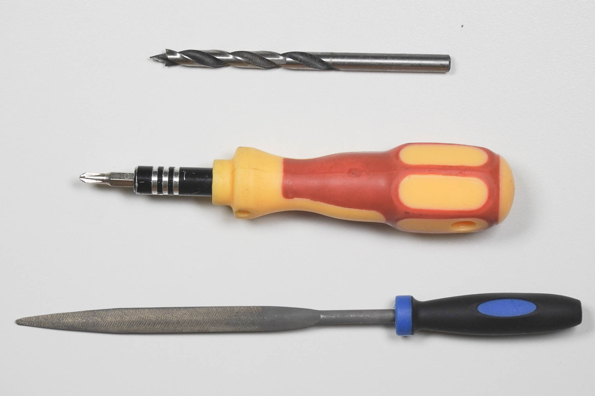 Ein 5-mm-Holzbohrer, ein Schraubendreher mit Kreuzschlitz-Bit und eine Flachfeile nebeneinander